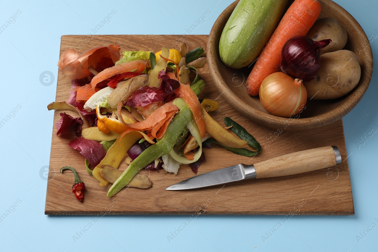 Photo of Different fresh vegetables with peels and knife on light blue background