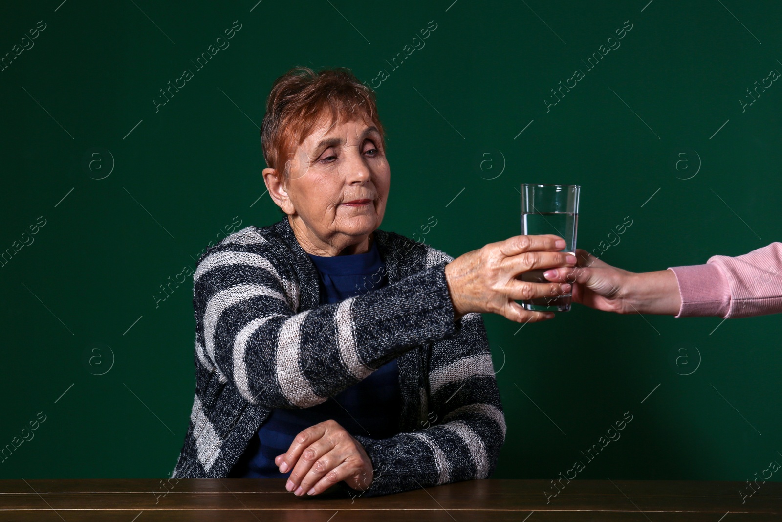 Photo of Poor senior woman taking glass of water at table against color background