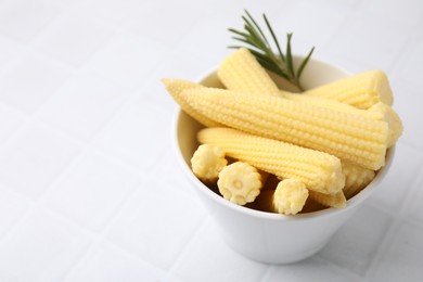 Photo of Tasty fresh yellow baby corns in bowl on white tiled table, closeup. Space for text