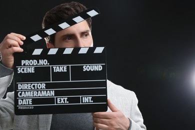 Actor holding clapperboard on black background, space for text