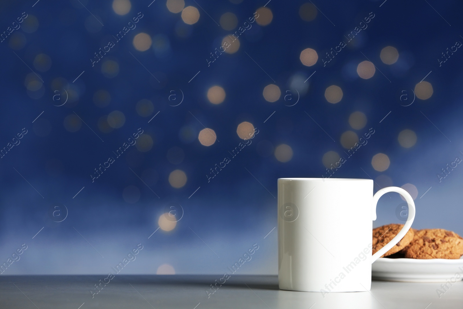 Photo of Cup of hot drink with tasty cookies on table against blurred lights, space for text. Bokeh effect