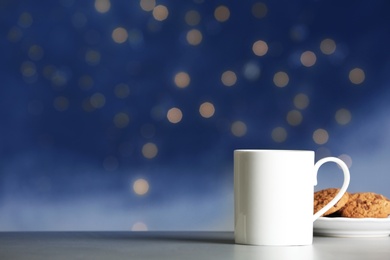 Cup of hot drink with tasty cookies on table against blurred lights, space for text. Bokeh effect