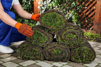 Photo of Gardener with grass sod rolls on backyard, closeup
