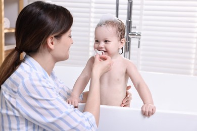 Mother bathing her cute little baby in tub at home