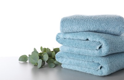 Photo of Fresh towels and eucalyptus branches on light grey table against white background