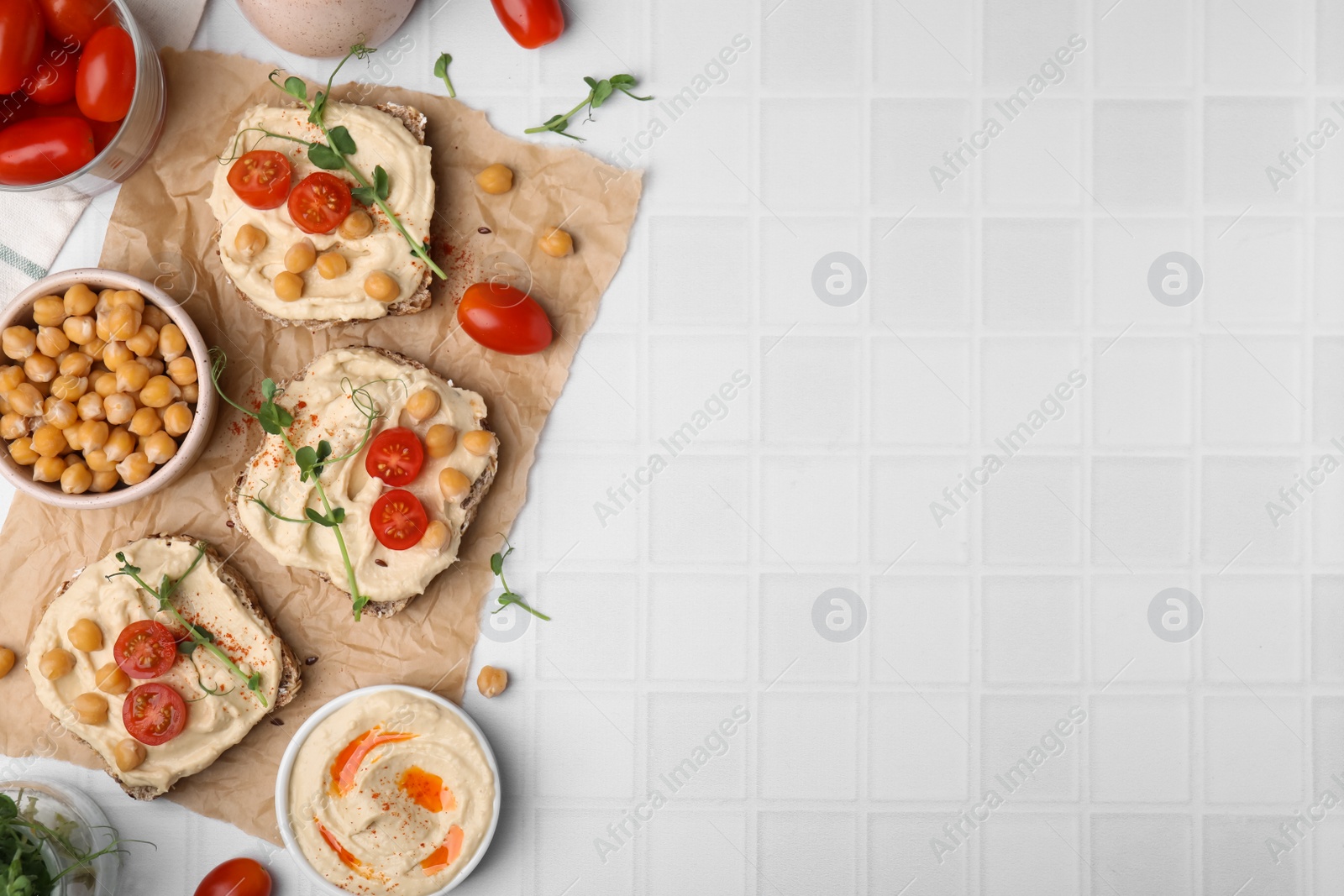 Photo of Delicious sandwiches with hummus and ingredients on white tiled table, flat lay. Space for text