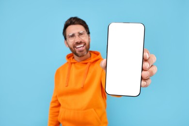 Photo of Handsome man showing smartphone in hand on light blue background, selective focus. Mockup for design