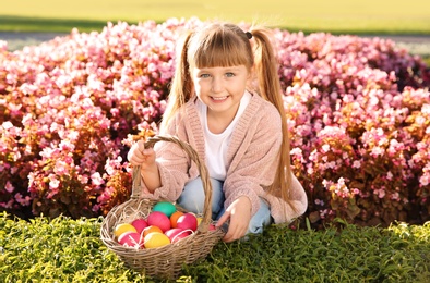 Photo of Cute little girl with basket of Easter eggs in park