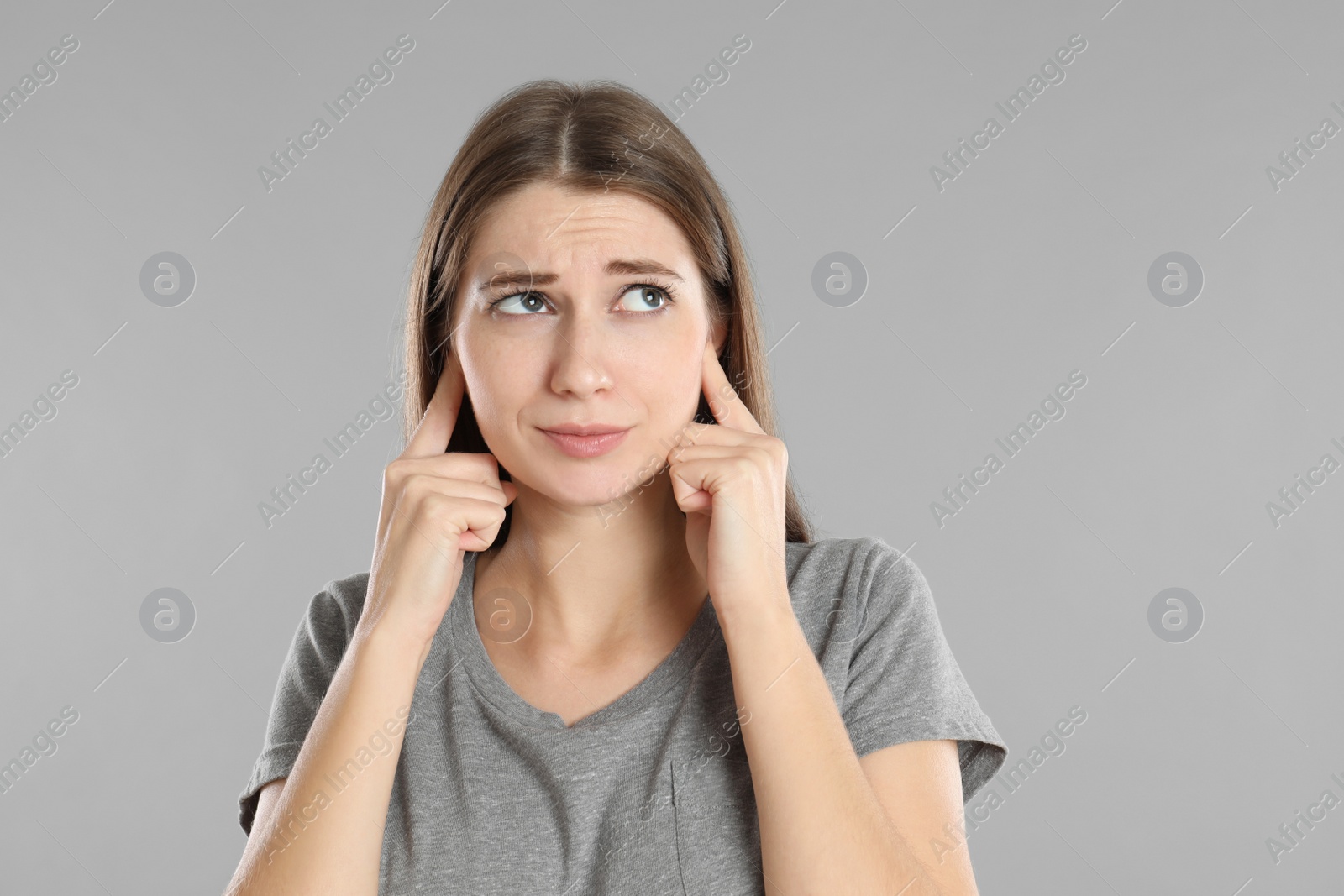 Photo of Emotional young woman covering her ears with fingers on grey background