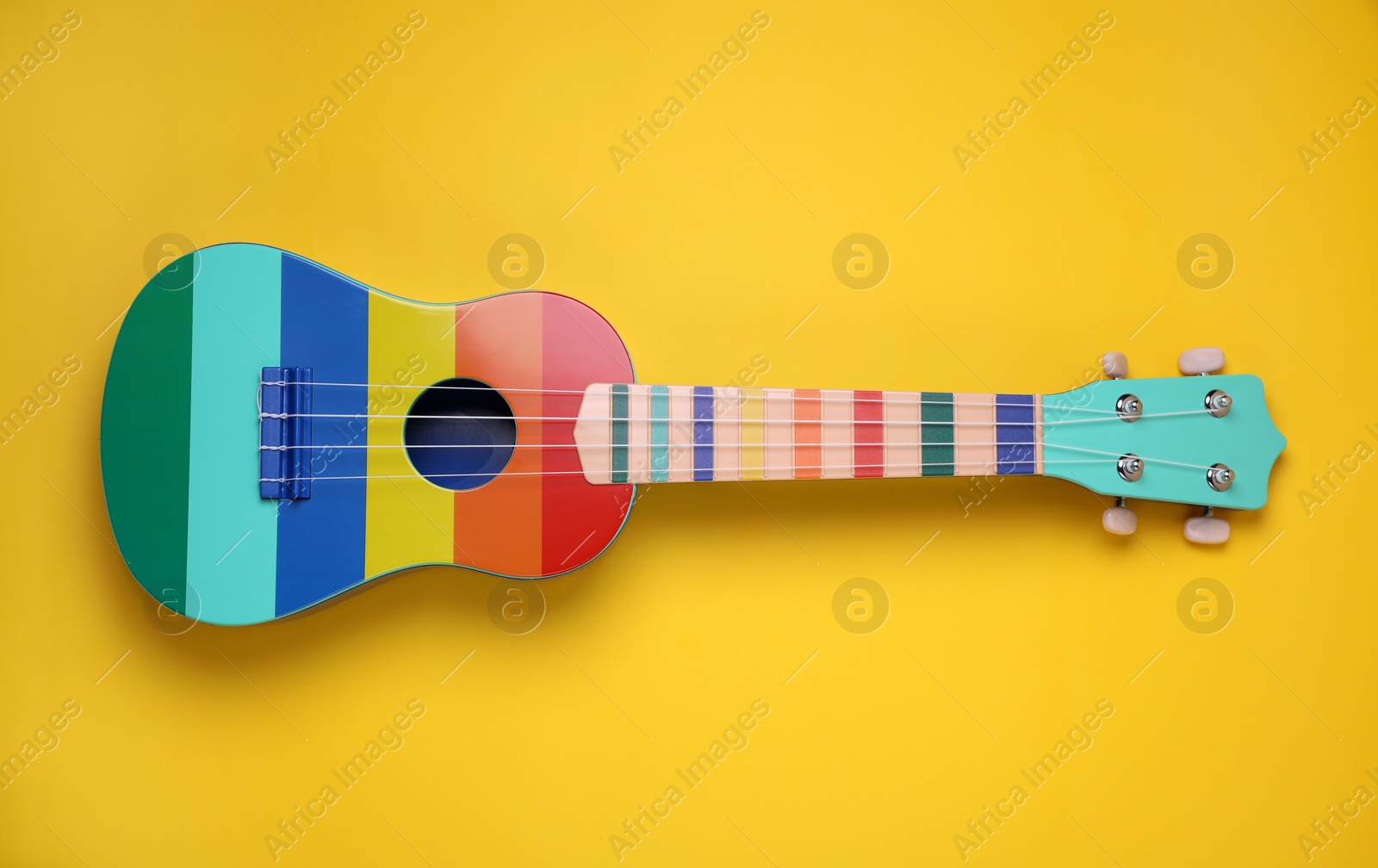 Photo of Colorful ukulele on yellow background, top view. String musical instrument