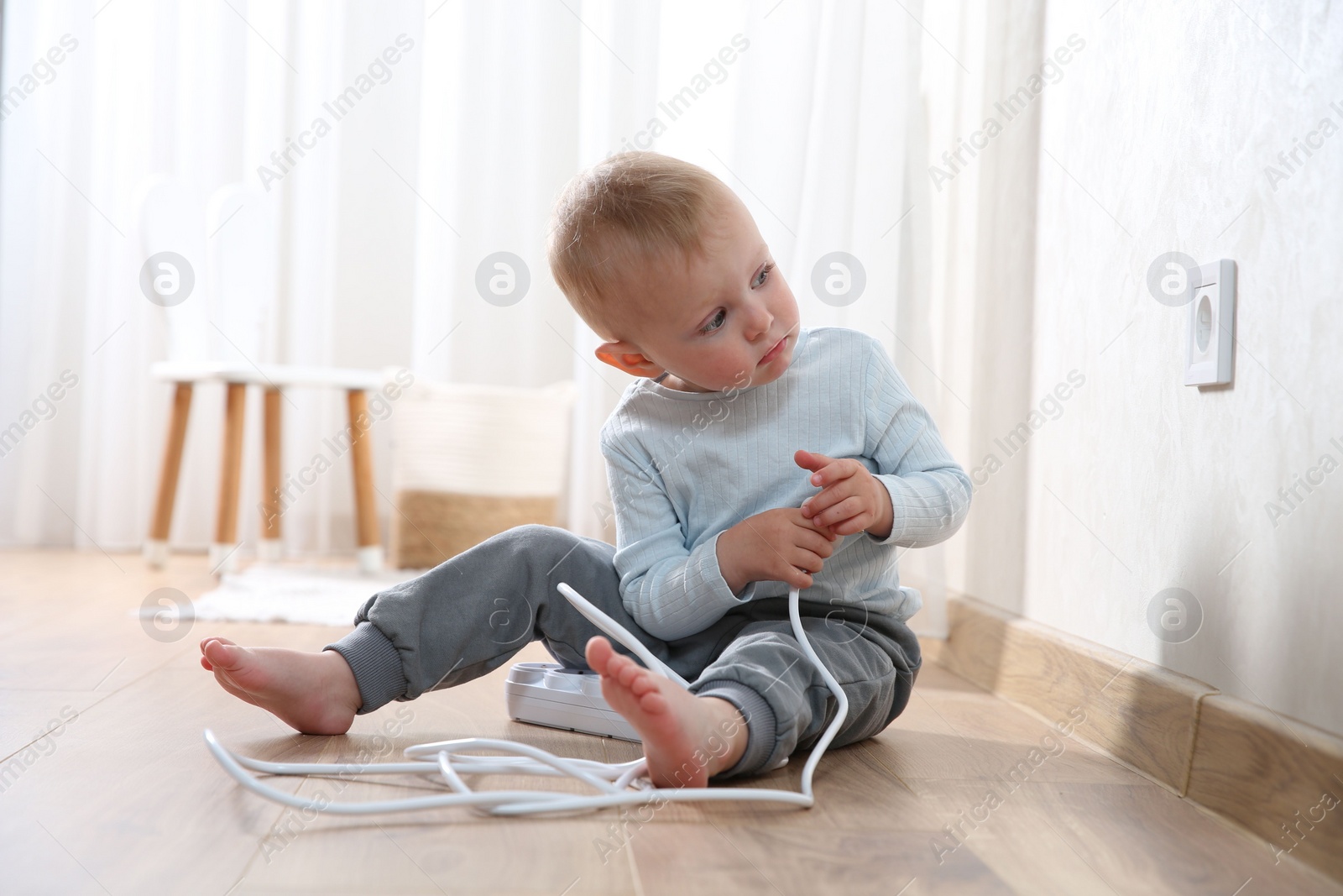 Photo of Little child playing with power strip plug near electrical socket at home. Dangerous situation