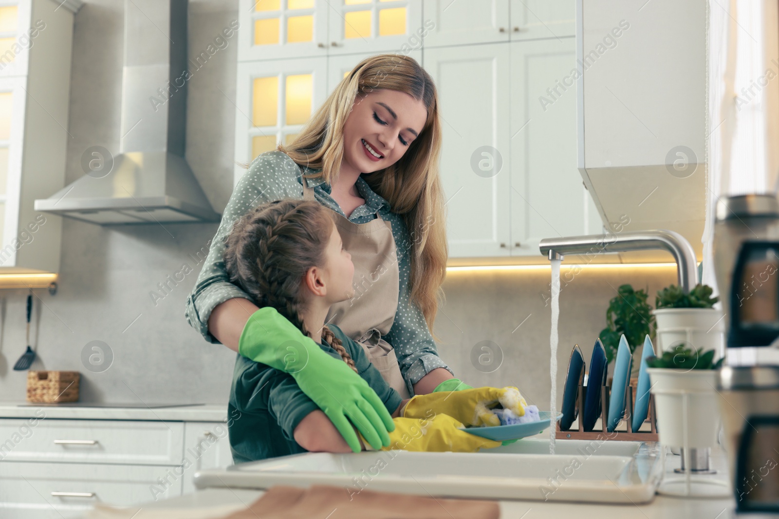 Photo of Mother and daughter in protective gloves washing plate above sink in kitchen