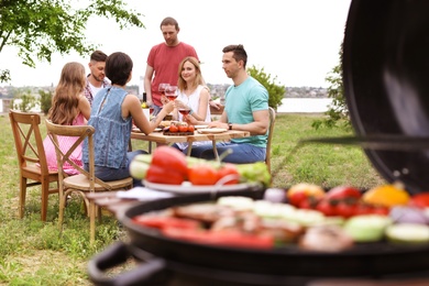 Photo of Young people with glasses of wine at table outdoors. Summer barbecue