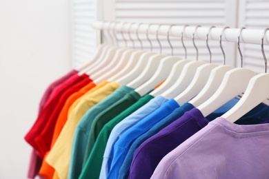 Photo of Rack with bright clothes in room. Rainbow colors