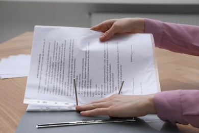 Woman putting punched pocket with document into folder at wooden table, closeup