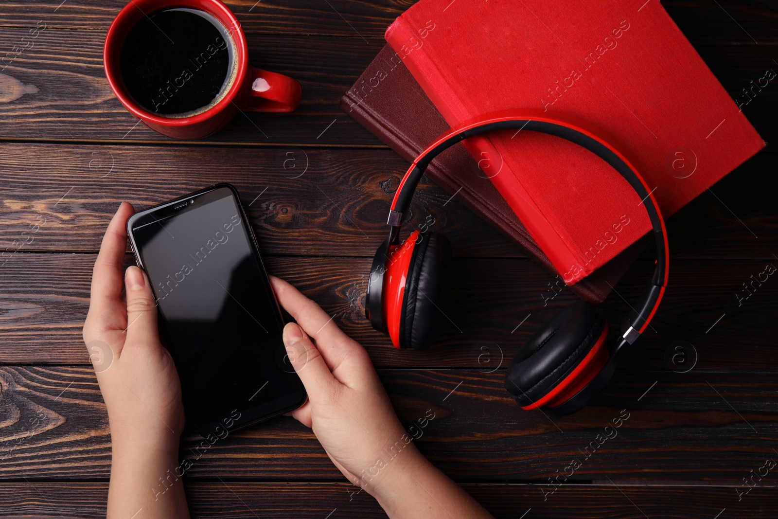 Photo of Woman holding mobile phone over wooden table with books, top view