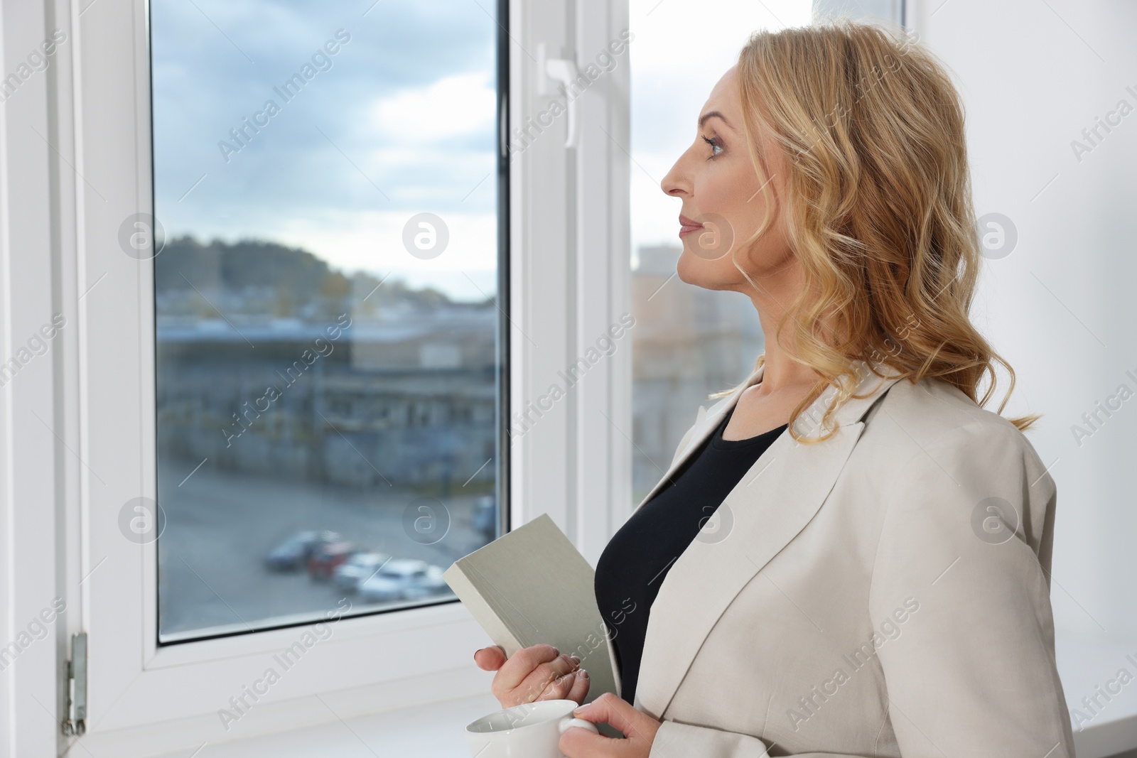 Photo of Lady boss with book and cup of drink near window indoors, space for text. Successful businesswoman