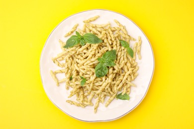 Plate of delicious trofie pasta with pesto sauce and basil leaves on yellow background, top view