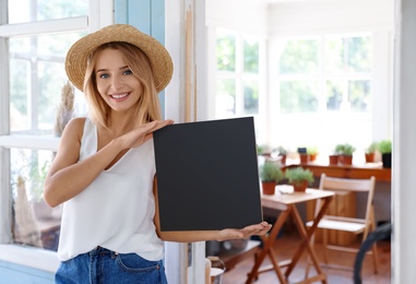 Photo of Young woman with blank chalkboard near home plant shop, space for text
