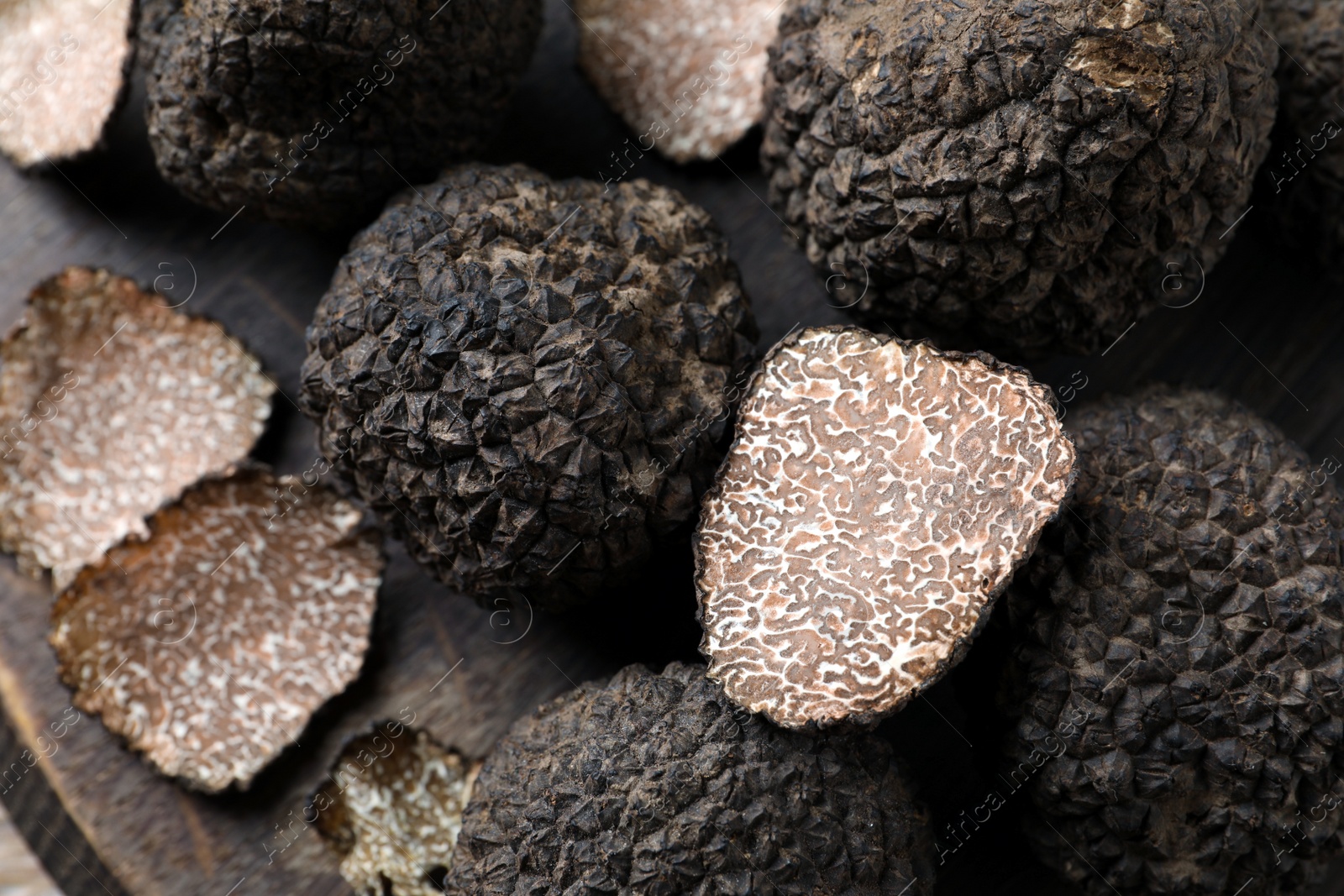 Photo of Whole and cut black truffles on wooden board, top view