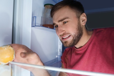 Man smelling stinky stale cheese in refrigerator