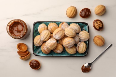 Photo of Homemade walnut shaped cookies with boiled condensed milk on white marble table, flat lay