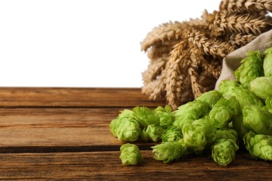 Photo of Overturned sack of hop flowers and wheat ears on wooden table against white background, space for text