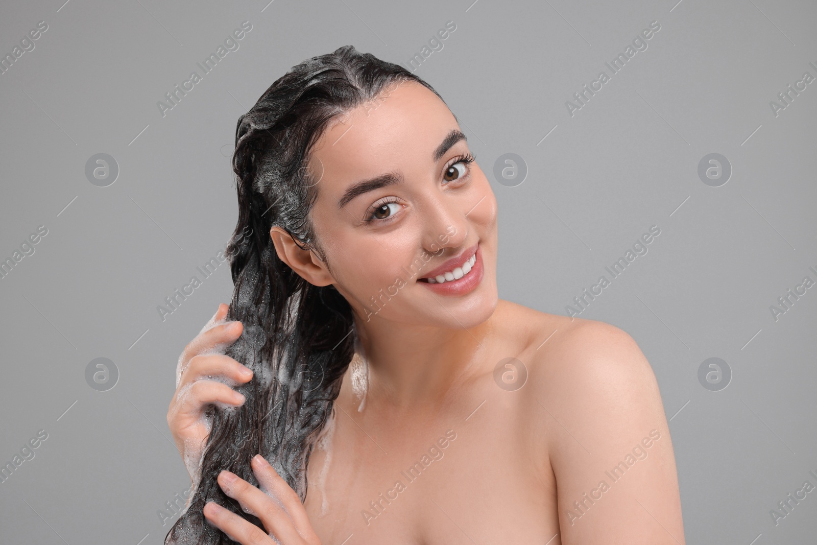 Photo of Portrait of beautiful happy woman washing hair on grey background