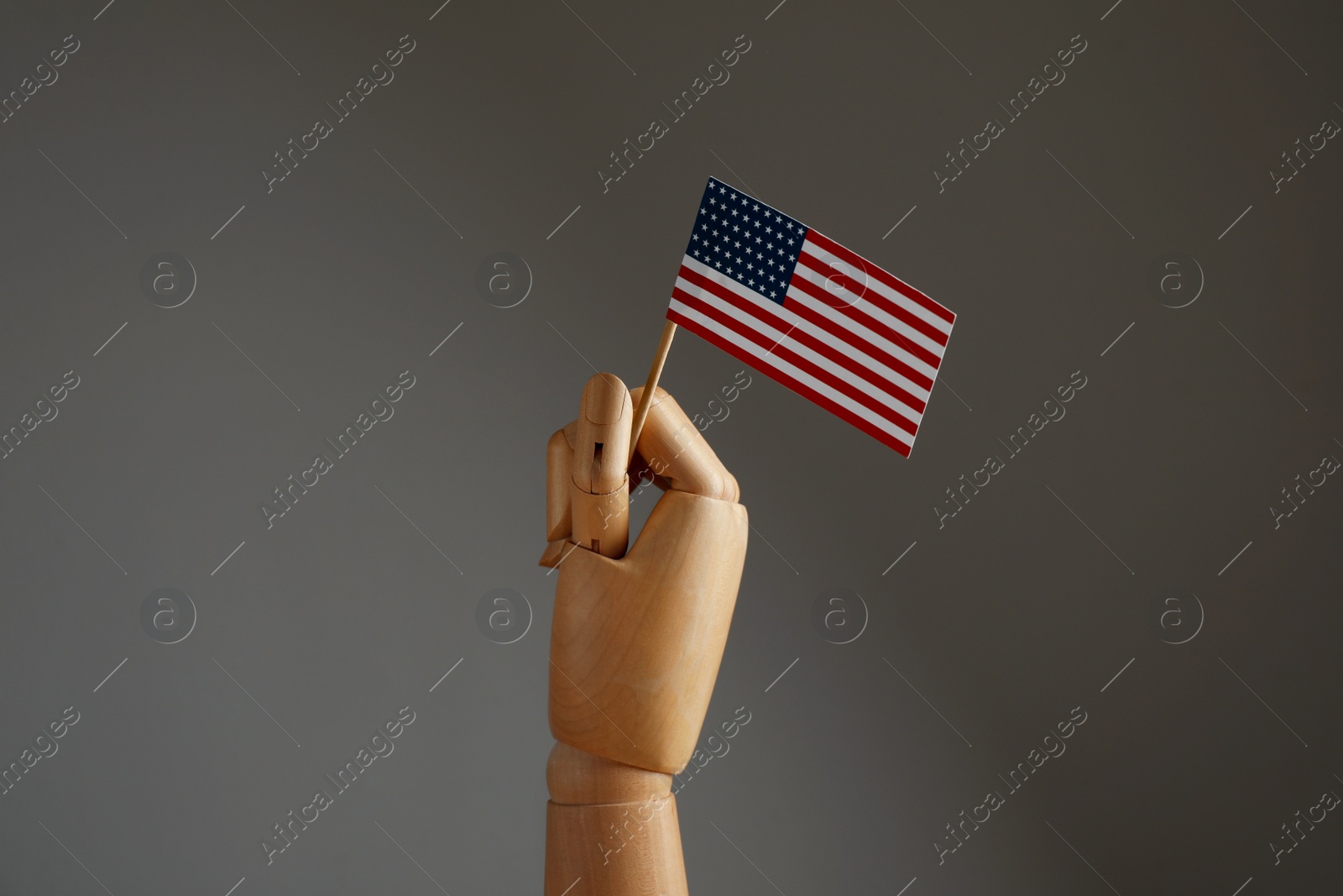 Photo of Wooden hand holding flag of USA on dark grey background