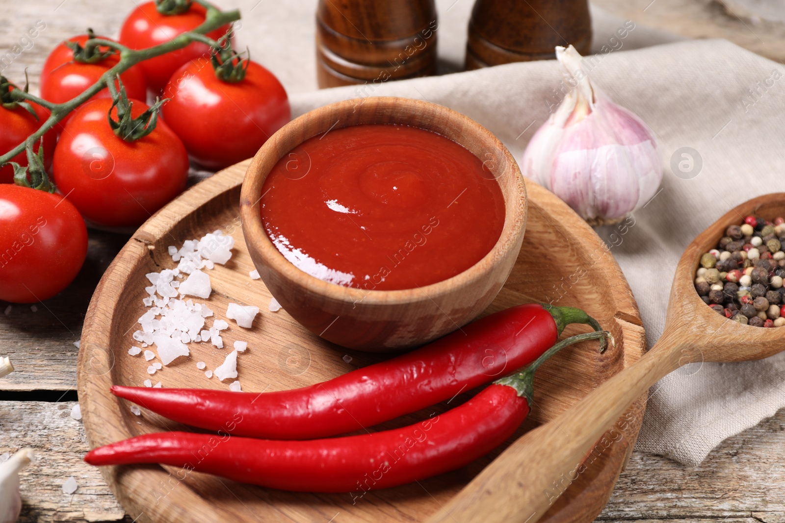 Photo of Delicious ketchup in bowl, chili pepper and spices on wooden table, closeup. Tomato sauce