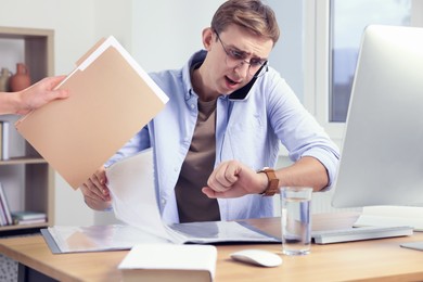 Deadline concept. Colleague giving folder with documents to overwhelmed man at desk in office