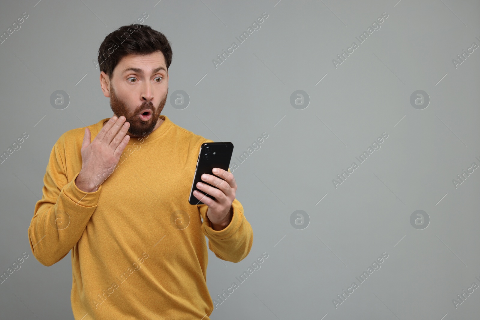 Photo of Surprised man with smartphone on grey background. Space for text