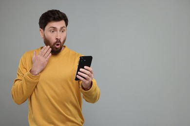 Photo of Surprised man with smartphone on grey background. Space for text