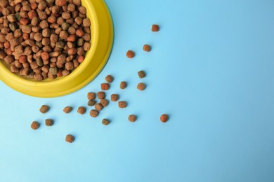 Dry pet food in feeding bowl on light blue background, flat lay. Space for text