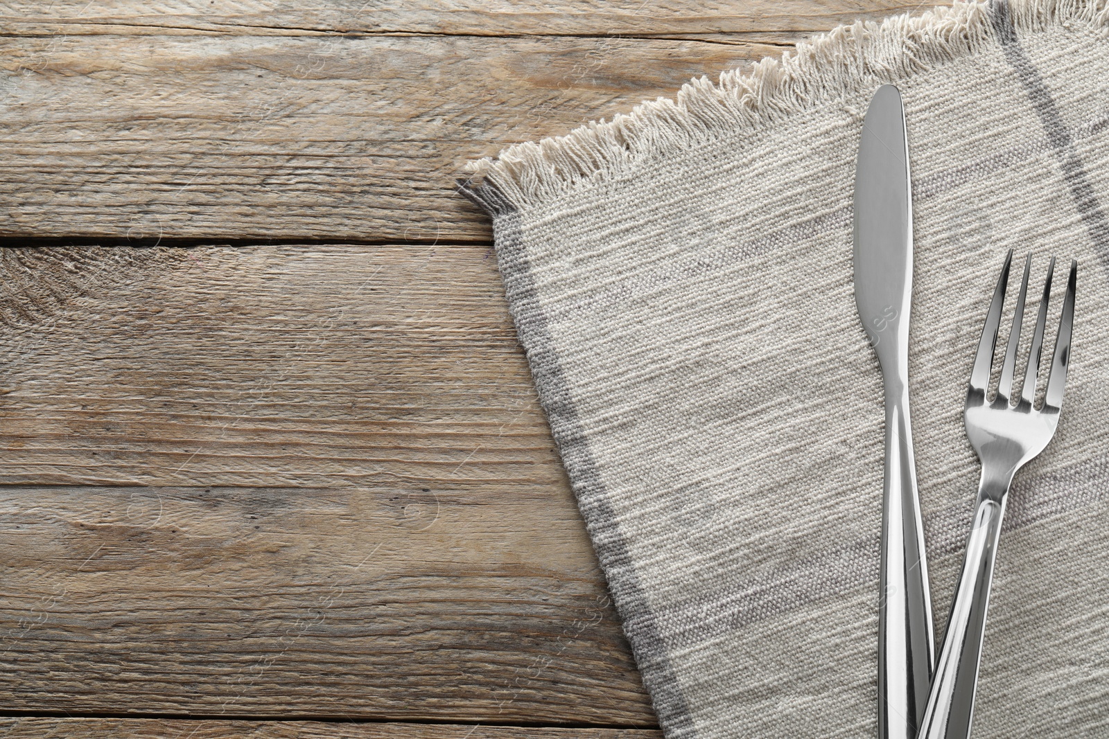 Photo of Fork, knife and napkin on wooden table, top view with space for text. Stylish shiny cutlery set