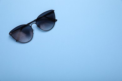 Stylish sunglasses on light blue background, top view. Space for text