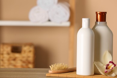 Photo of Bottles of shampoo, hairbrush and flower on wooden table in bathroom, space for text