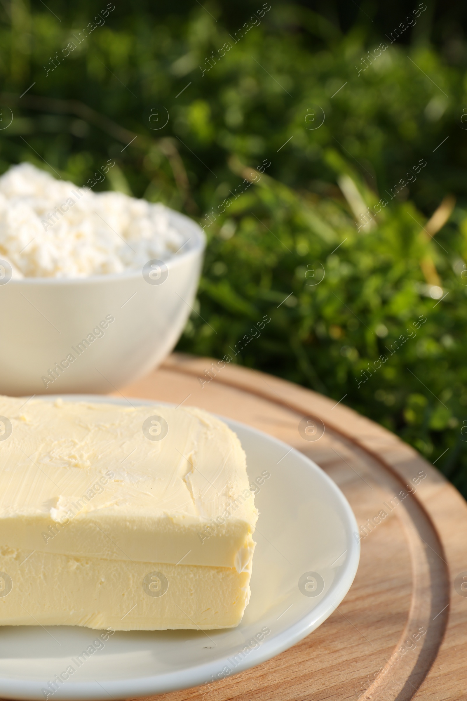 Photo of Wooden tray with tasty homemade butter and dairy products on grass outdoors, closeup