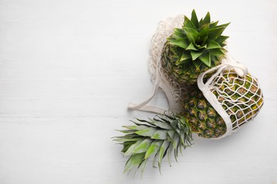 Photo of Net bag with delicious ripe pineapples on white wooden table, top view. Space for text