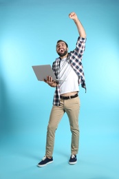 Emotional young man with laptop celebrating victory on color background