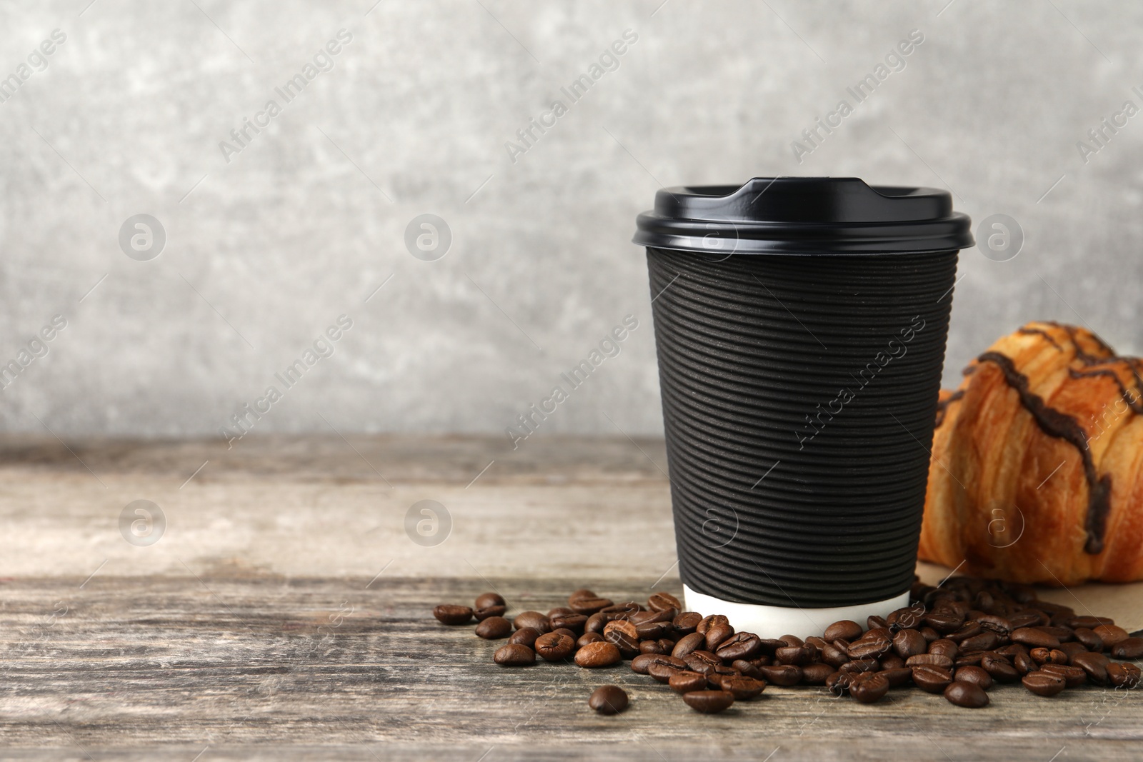 Photo of Coffee to go. Paper cup with tasty drink, croissant and beans on wooden table. Space for text