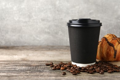 Coffee to go. Paper cup with tasty drink, croissant and beans on wooden table. Space for text