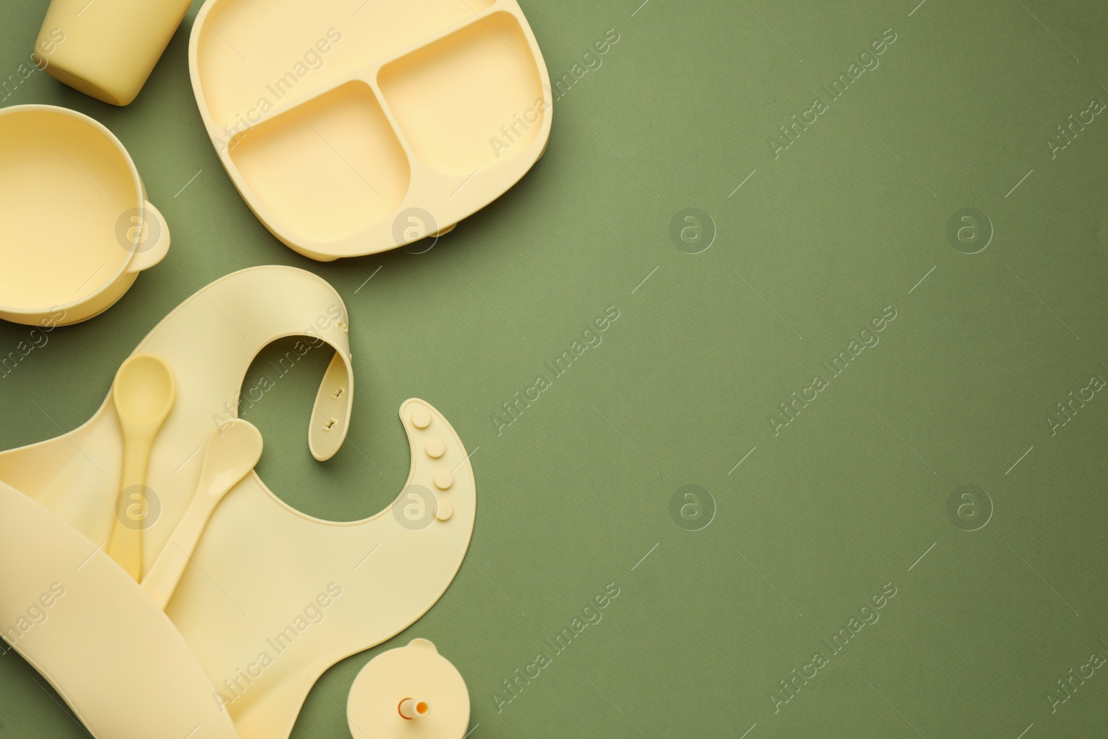 Photo of Flat lay composition with baby feeding accessories and bib on green background, space for text