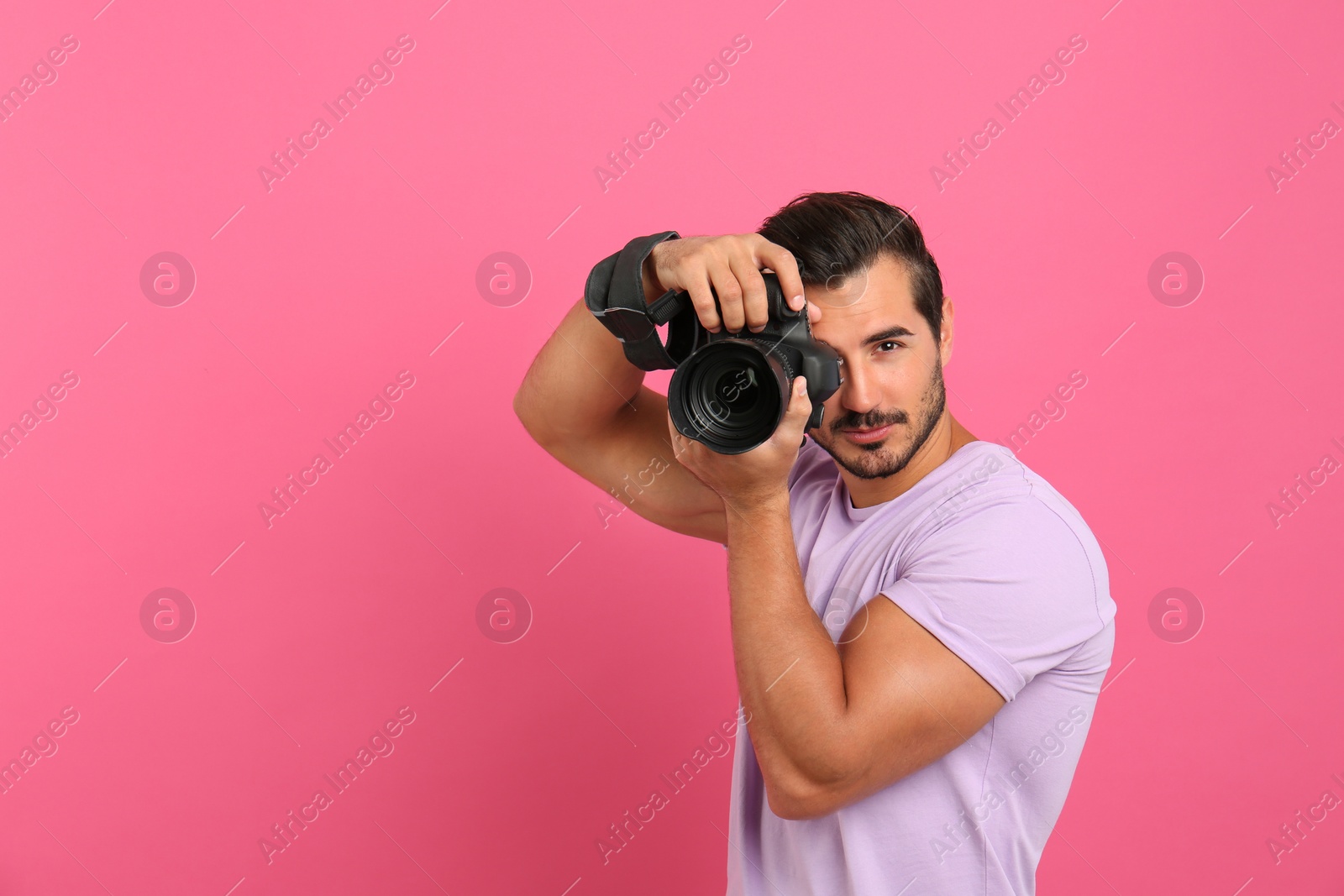 Photo of Young professional photographer taking picture on pink background. Space for text