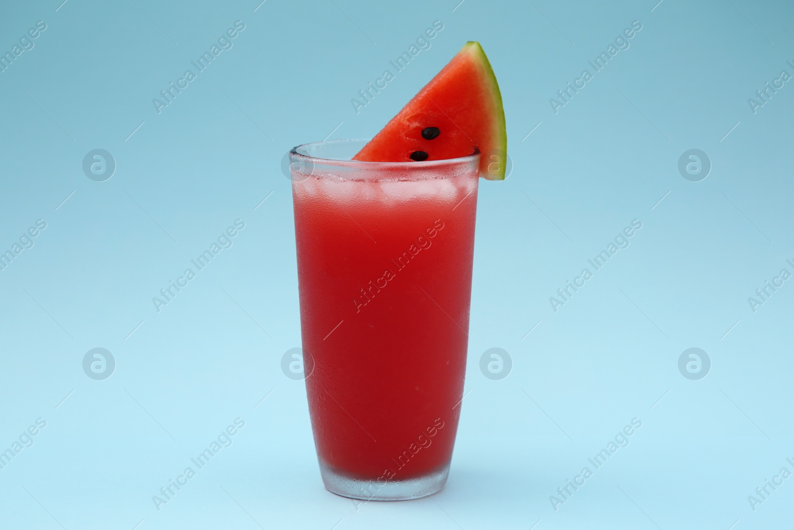 Photo of Delicious drink with ice cubes and piece of fresh watermelon on light blue background