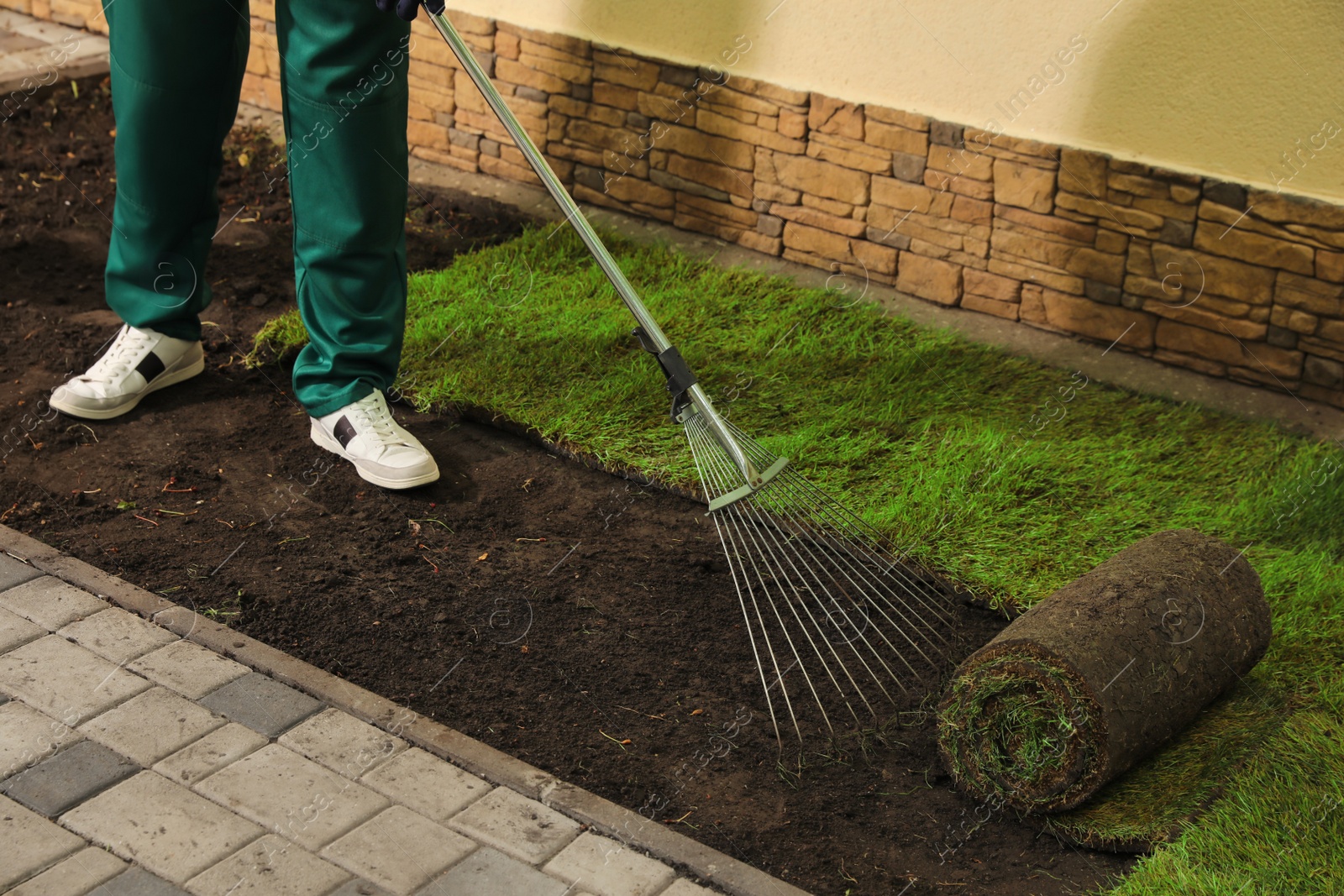 Photo of Worker leveling soil before laying grass sod at backyard, closeup