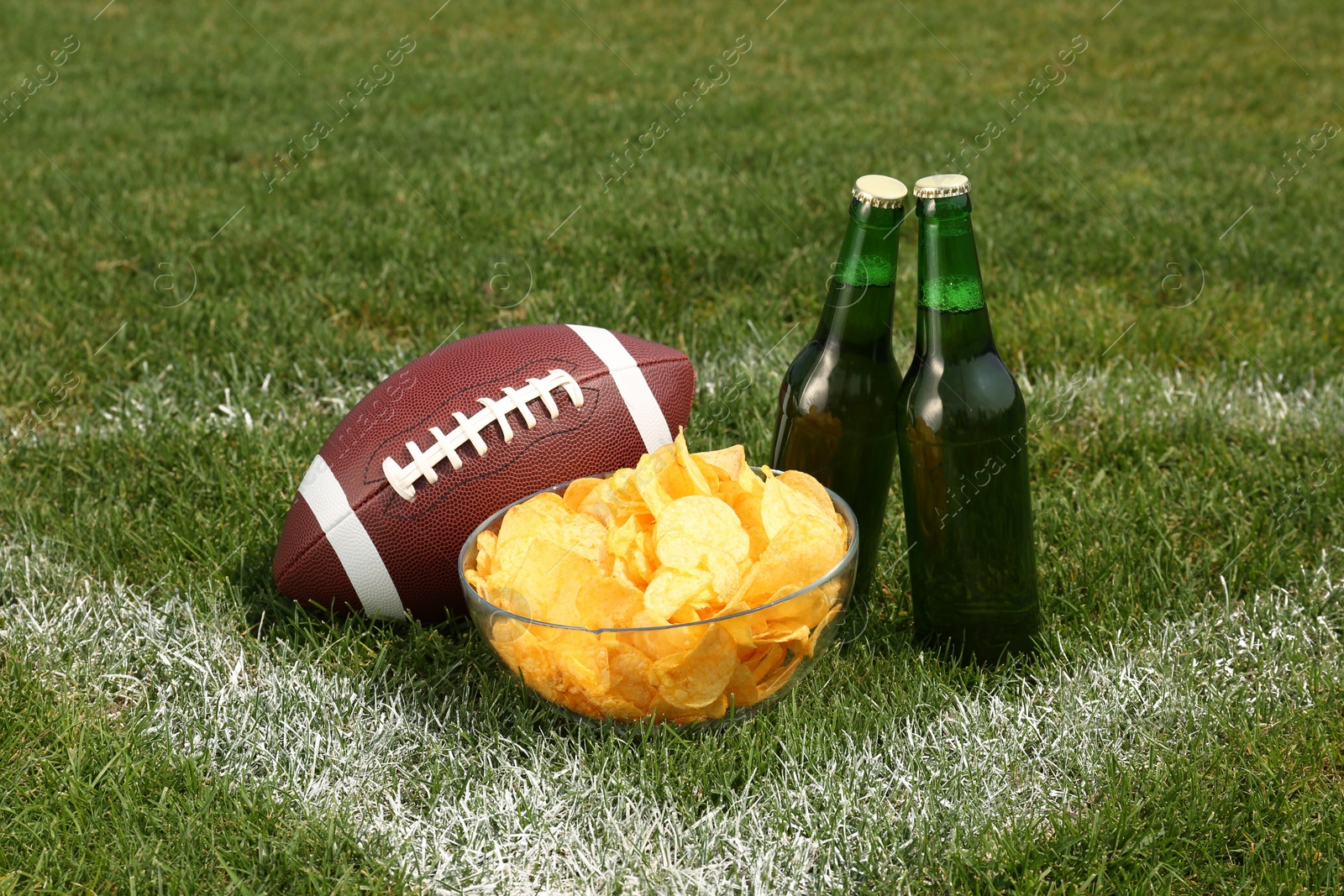 Photo of American football ball with beer and chips on green field grass outdoors