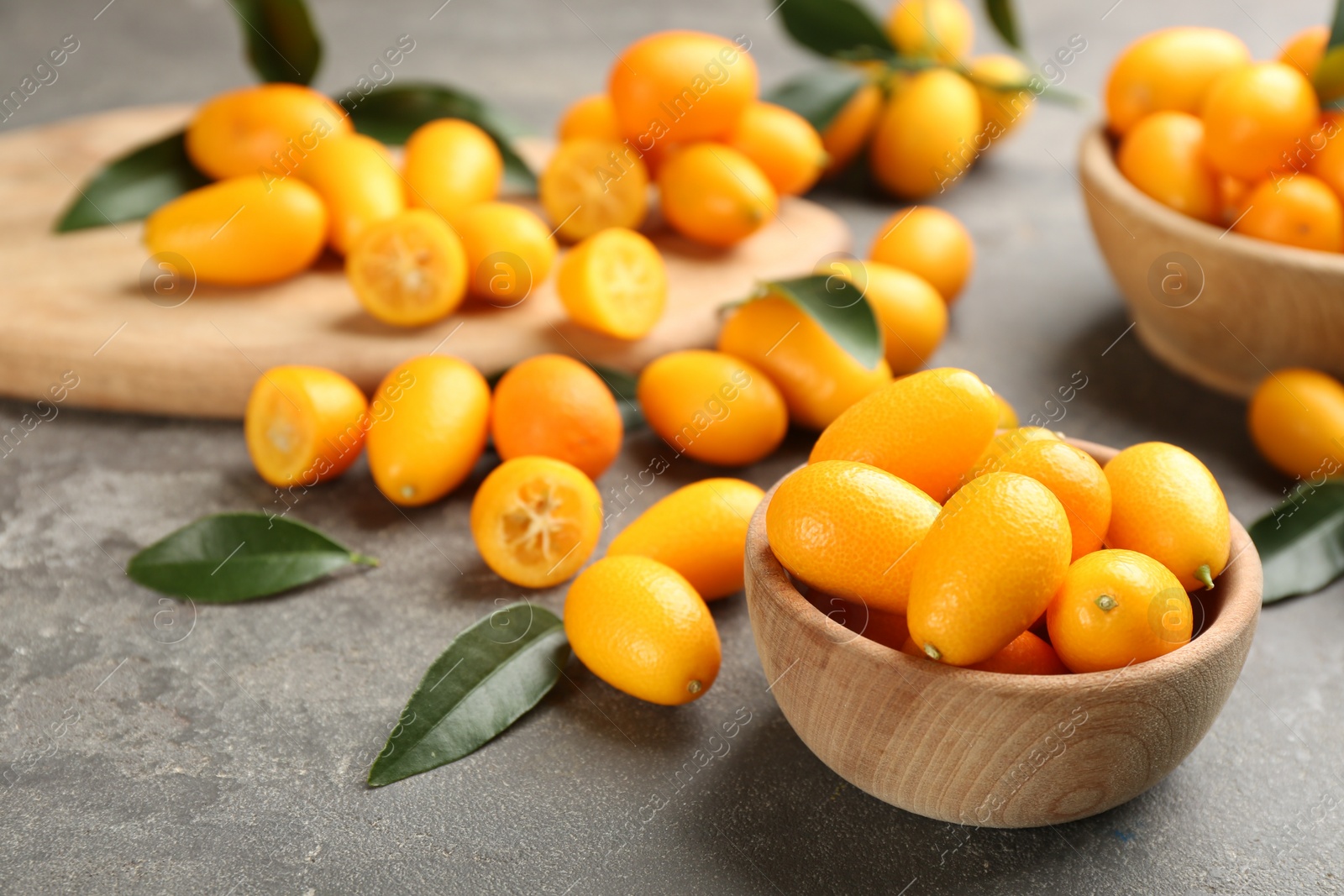 Photo of Fresh ripe kumquats in bowl on grey table, space for text