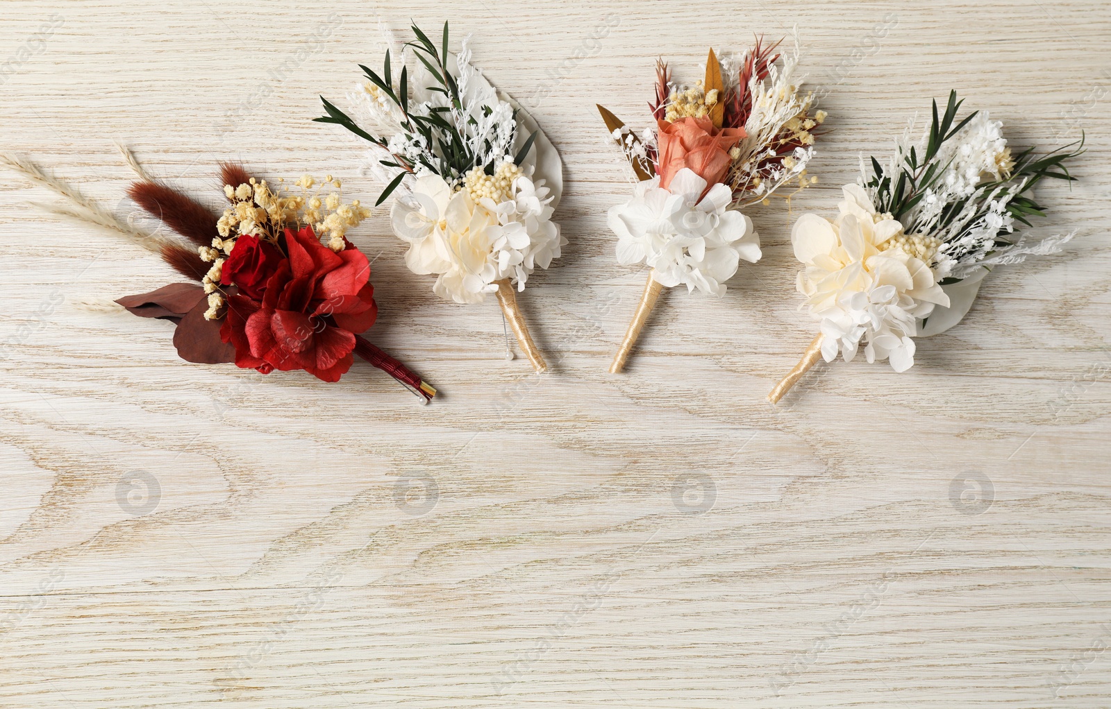 Photo of Stylish boutonnieres on white wooden table, flat lay. Space for text