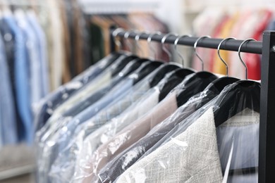 Dry-cleaning service. Many different clothes in plastic bags hanging on rack indoors, closeup